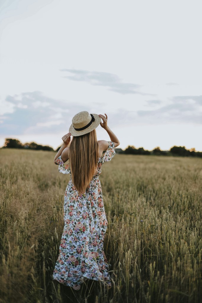 Feminine girl wearing floral dress and hat standing calmly on farm – gentle image of faith-based encouragement for worried hearts seeking peace through scripture and prayer