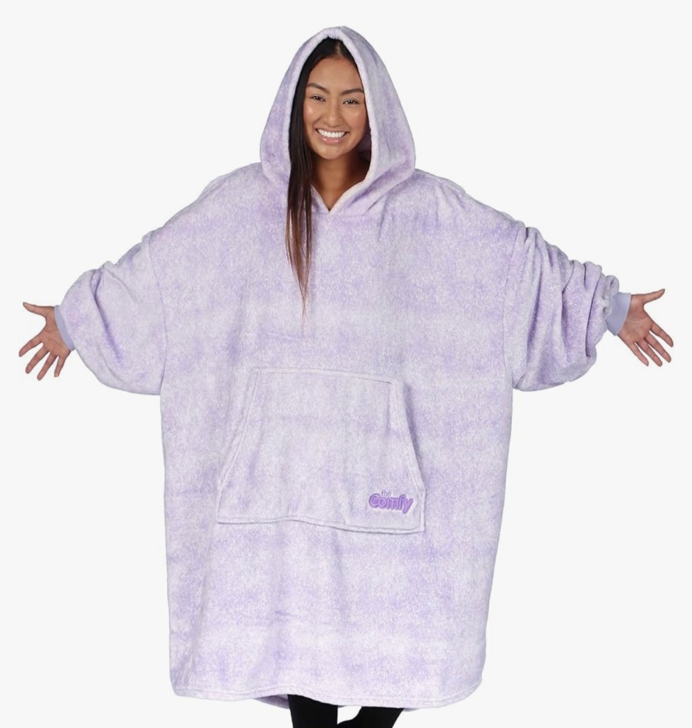 Young woman smiling and posing with arms outstretched while wearing The Comfy Original oversized wearable blanket hoodie in soft lavender purple. This cozy sherpa-lined blanket sweatshirt features a large hood, oversized sleeves, and a giant front pocket—perfect for cozy girl essentials, lounging at home, or ultimate winter comfort as a wearable blanket. Perfect for when you’re dealing with Spiritual Warfare and Emotional Health.