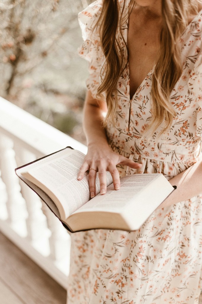 Young woman in floral dress gently holding an open Bible - Inspiring Christian devotionals for women overcoming fear, with Bible verses for women with anxiety and heartfelt encouragement to find peace in God's Word